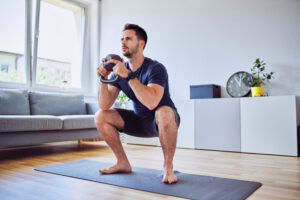 Training at home young man doing squats with kettlebell weights